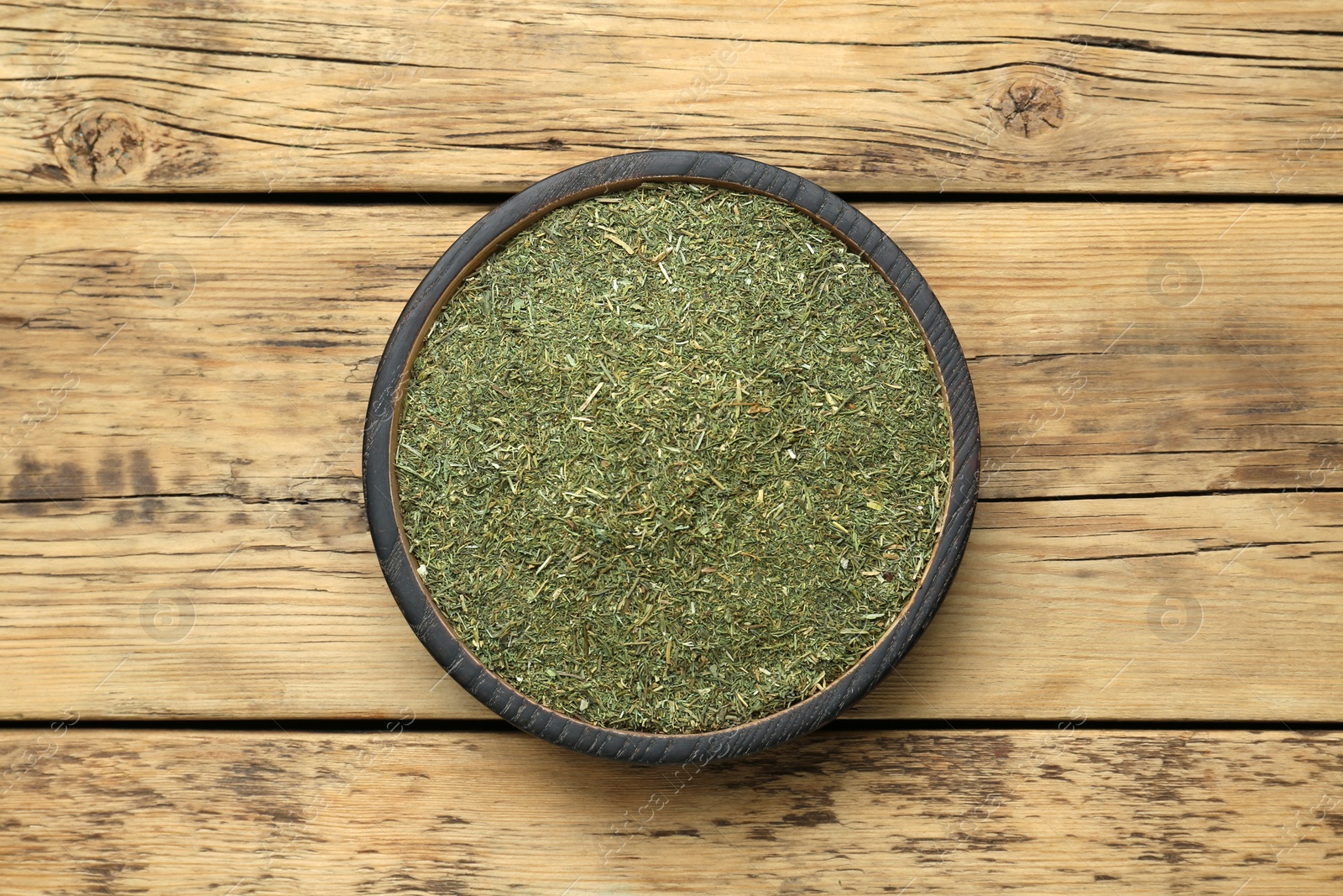 Photo of Dried dill in bowl on wooden table, top view