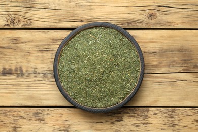 Dried dill in bowl on wooden table, top view