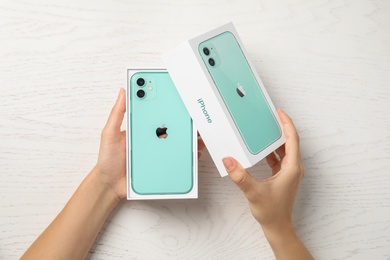 MYKOLAIV, UKRAINE - JULY 10, 2020: Woman opening box with new modern Iphone 11 Green at white wooden table, top view