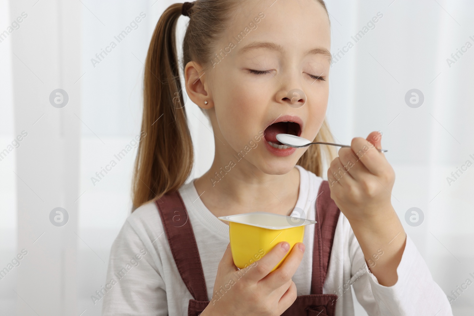 Photo of Cute little girl enjoying tasty yogurt indoors