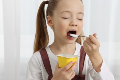 Photo of Cute little girl enjoying tasty yogurt indoors