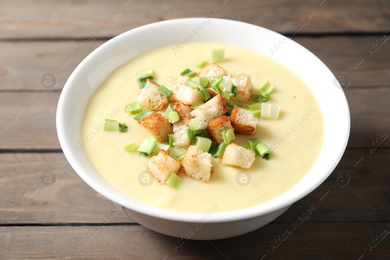 Photo of Tasty potato soup with croutons and green onion in bowl on wooden table