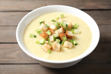 Photo of Tasty potato soup with croutons and green onion in bowl on wooden table