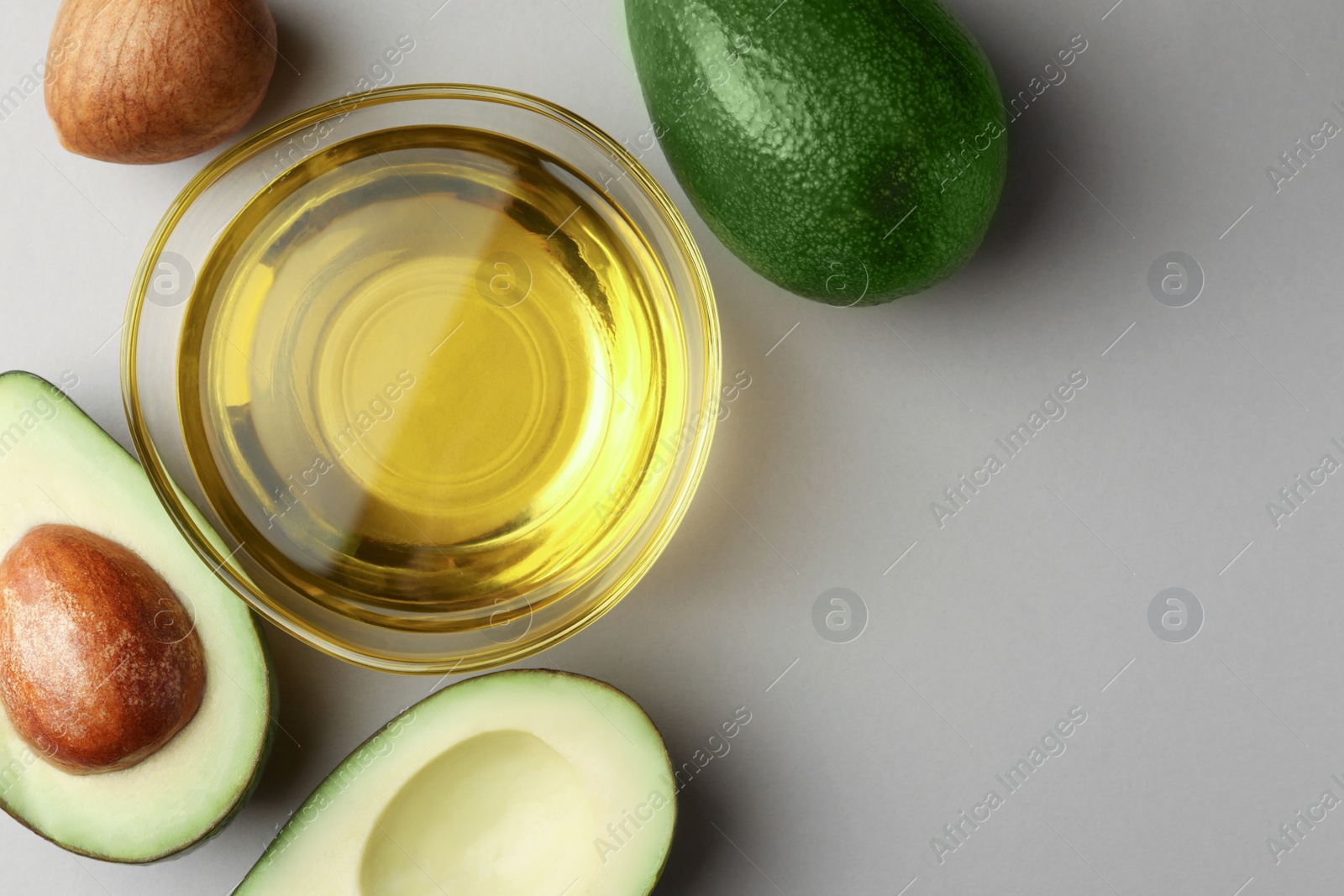 Photo of Cooking oil in bowl and fresh avocados on light grey background, flat lay. Space for text