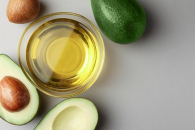 Photo of Cooking oil in bowl and fresh avocados on light grey background, flat lay. Space for text