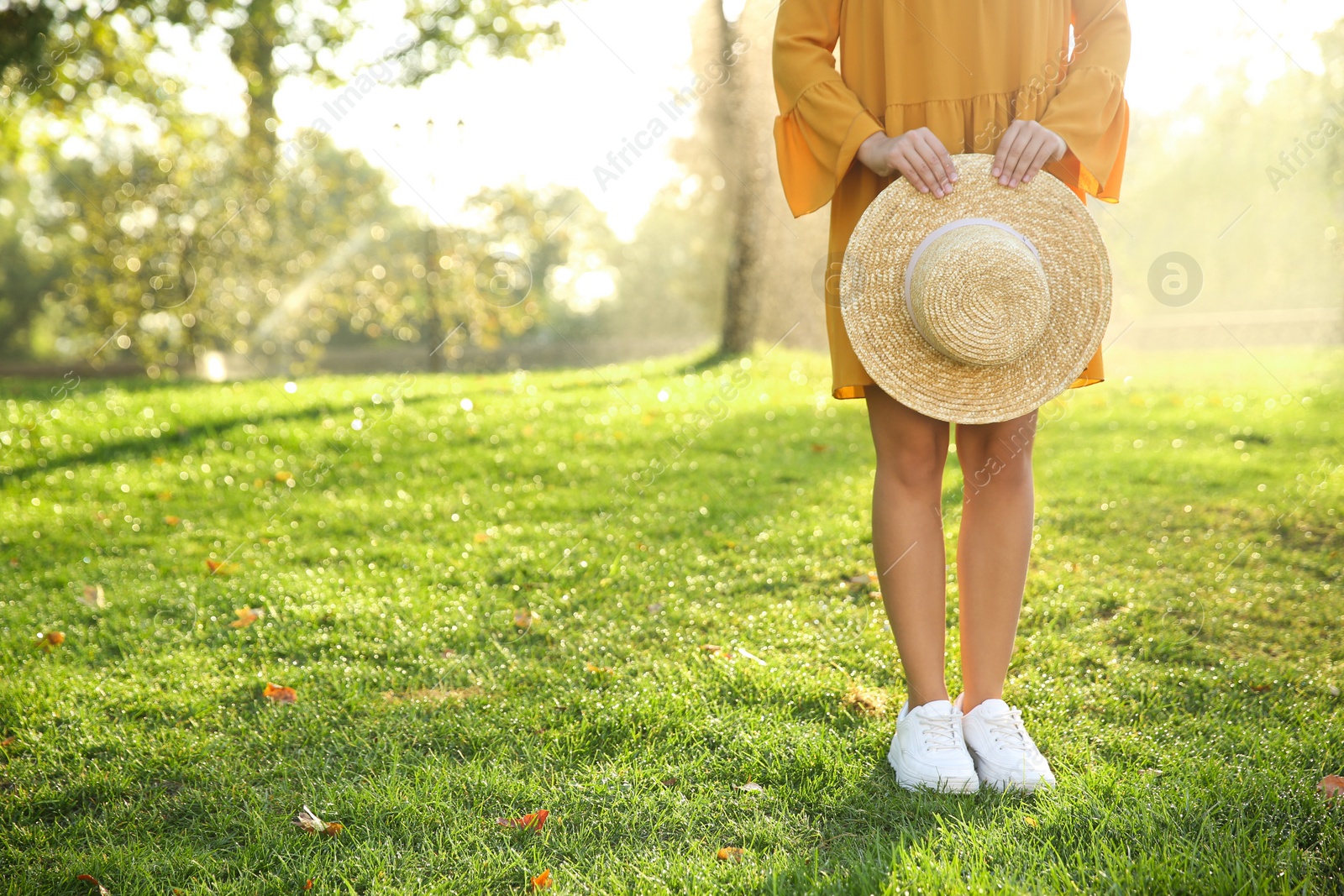 Photo of Woman wearing stylish yellow dress and sneakers with straw hat in park, closeup