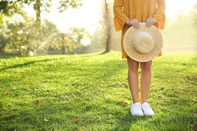 Photo of Woman wearing stylish yellow dress and sneakers with straw hat in park, closeup