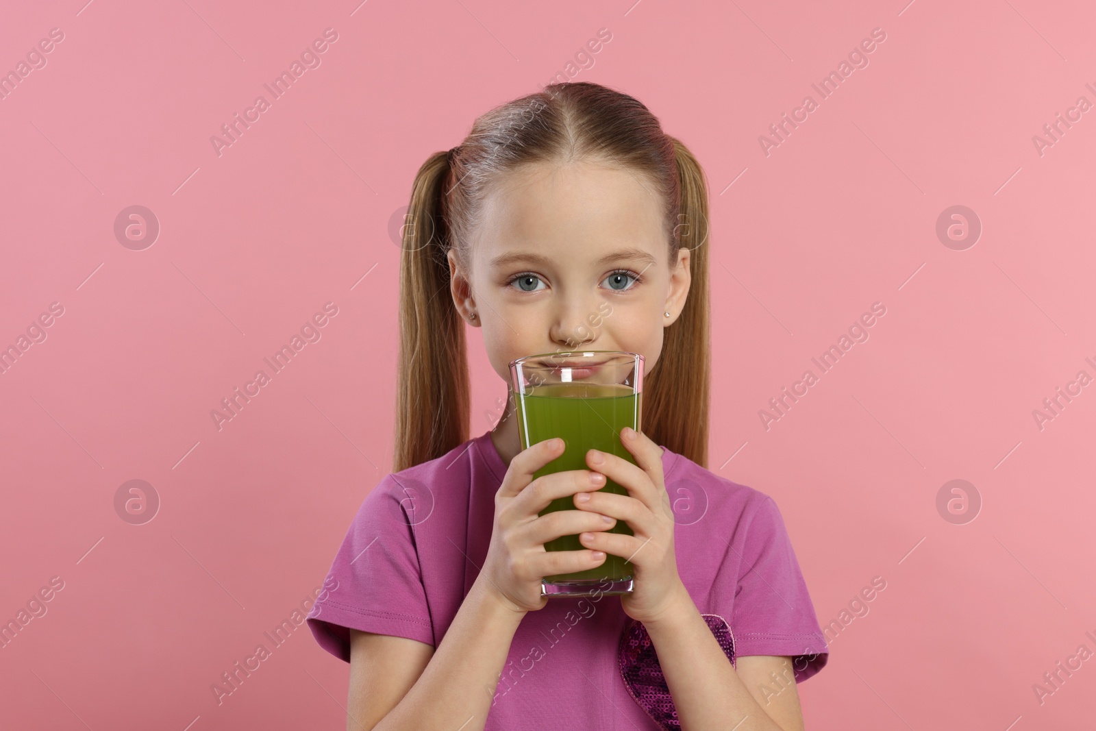 Photo of Cute little girl with glass of fresh juice on pink background