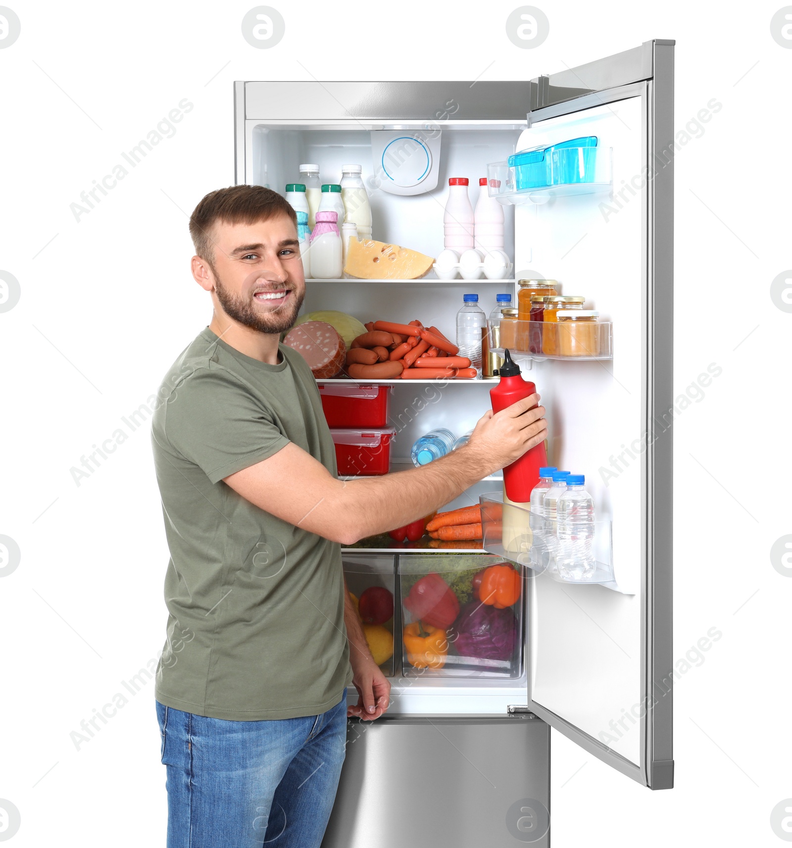 Photo of Young man taking bottle of ketchup from refrigerator on white background