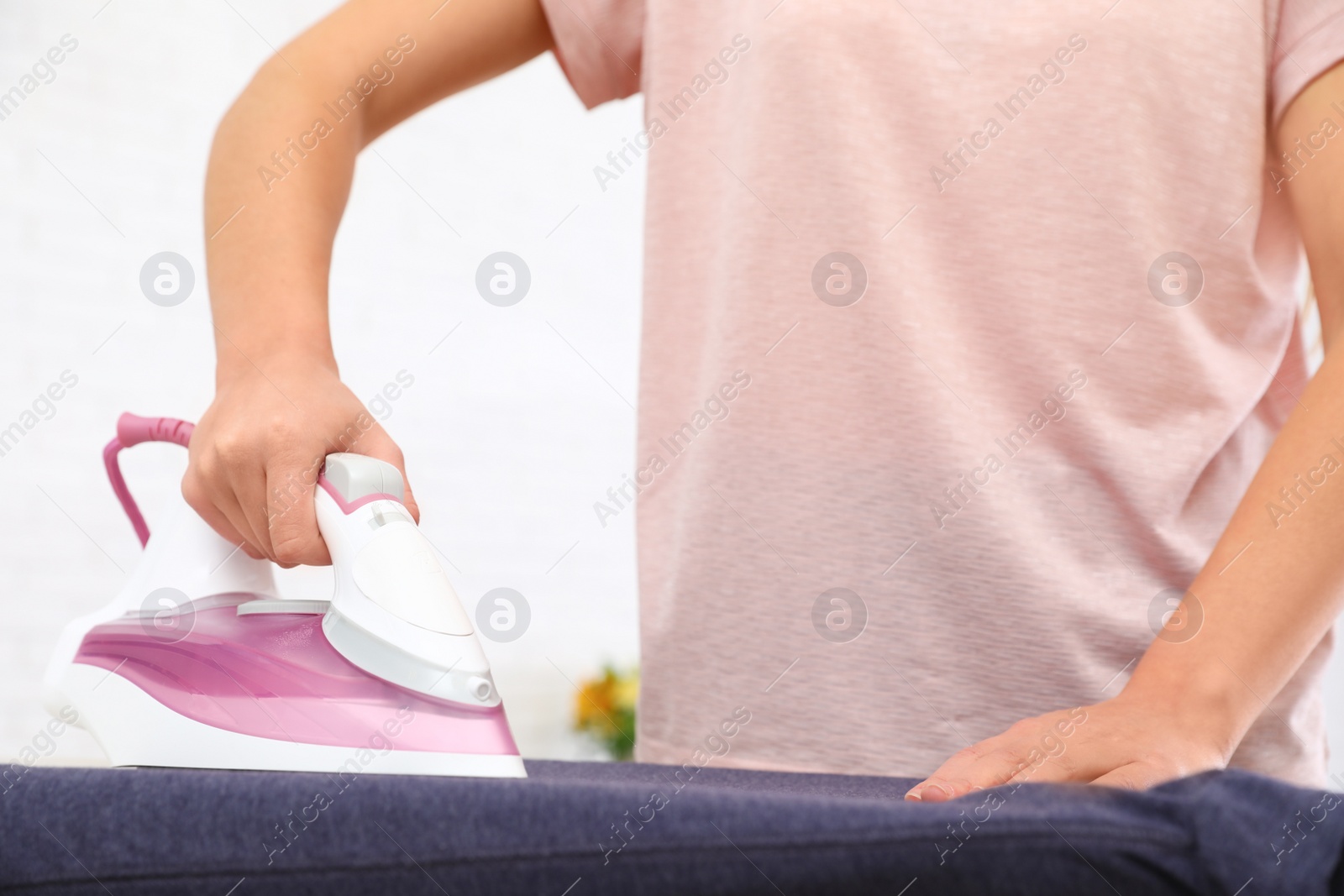 Photo of Young woman ironing clothes on board at home, closeup