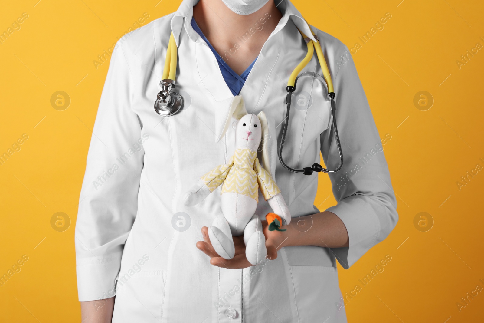 Photo of Pediatrician with toy bunny and stethoscope on yellow background, closeup