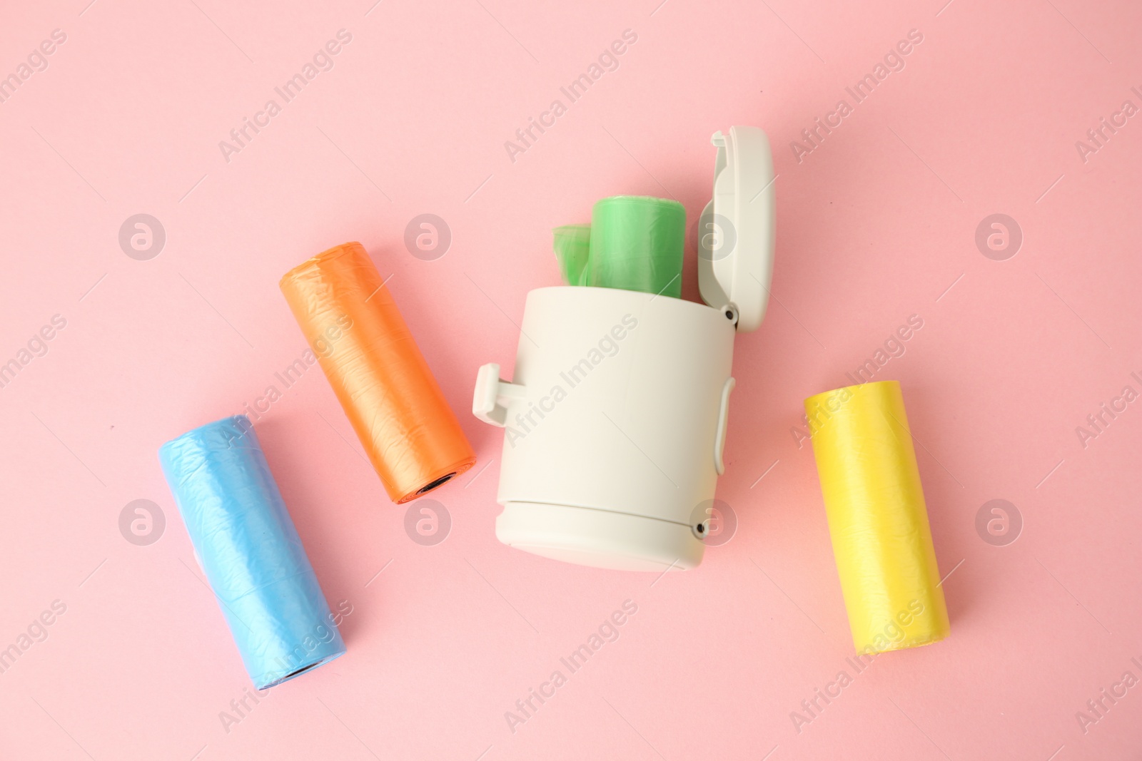 Photo of Dog waste bags and dispenser on pink background, flat lay