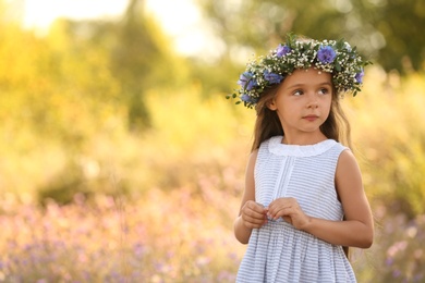 Photo of Cute little girl wearing flower wreath outdoors, space for text. Child spending time in nature