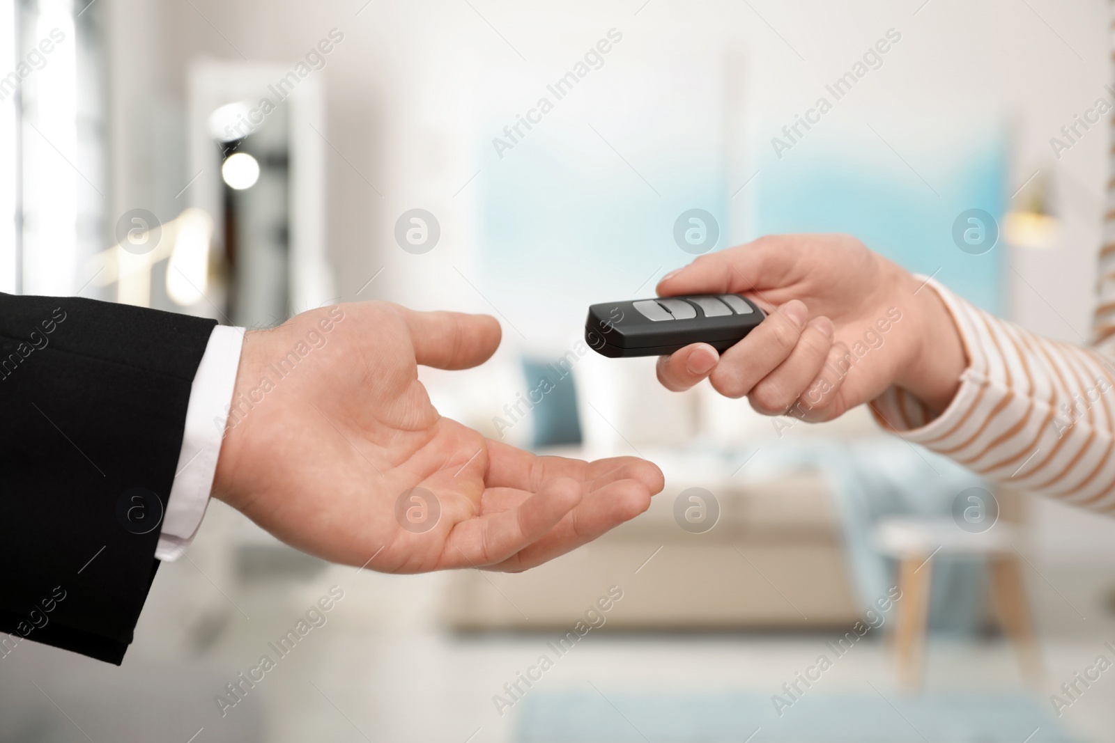 Photo of Woman giving car smart key to man indoors, closeup