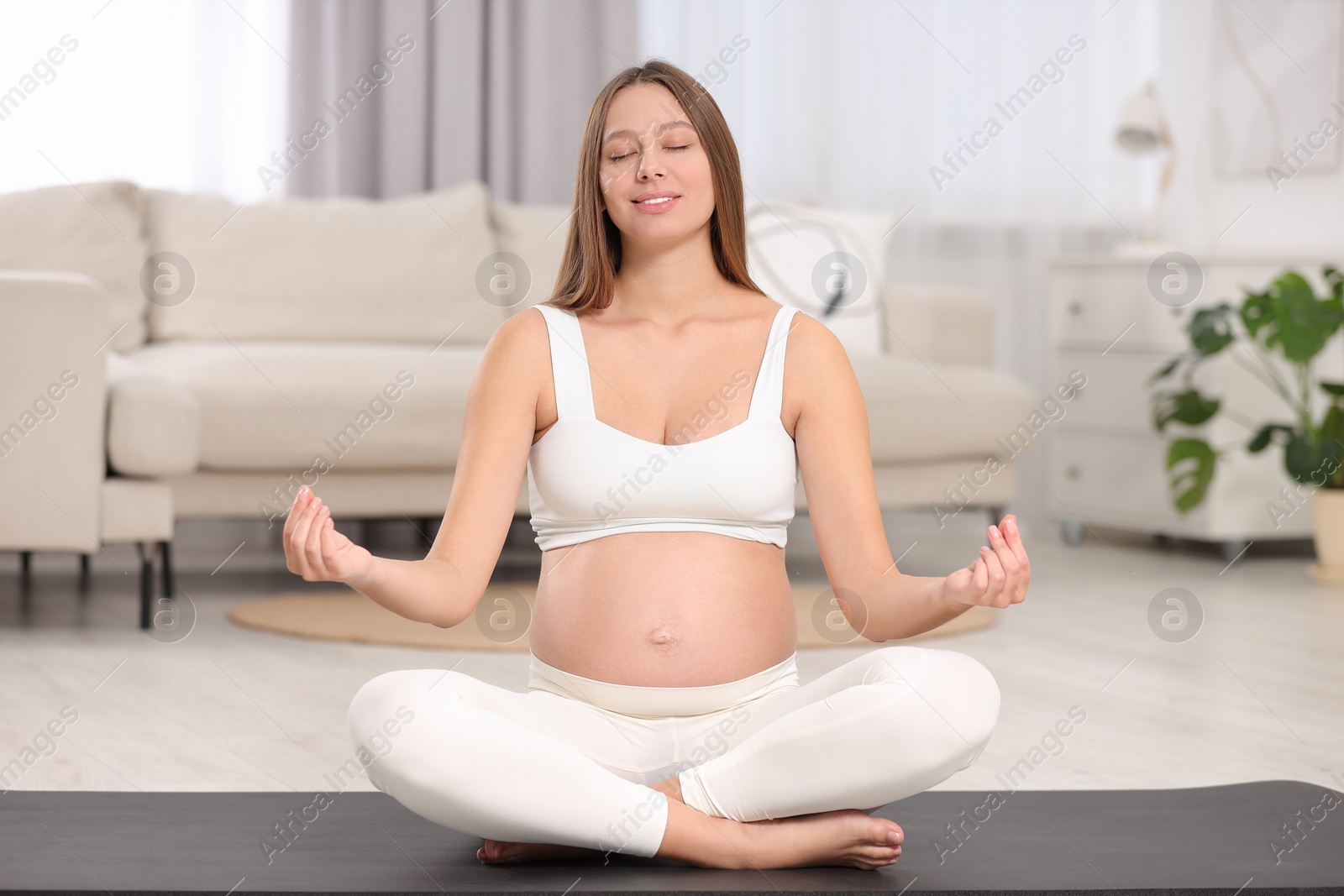 Photo of Pregnant woman meditating on yoga mat at home