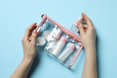 Photo of Cosmetic travel kit. Woman putting small bottle with personal care product into plastic bag against light blue background, top view