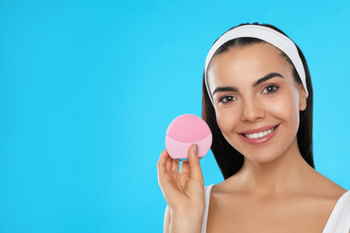 Photo of Young woman holding facial cleansing brush on light blue background, space for text. Washing accessory