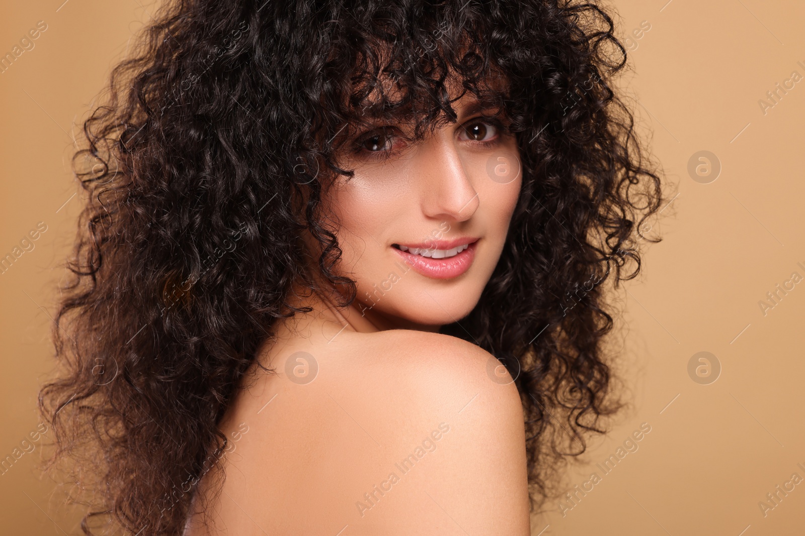 Photo of Beautiful young woman with long curly hair on beige background