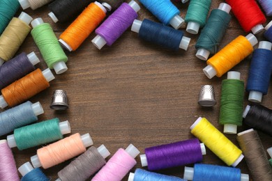 Frame made of colorful threads and sewing thimbles on wooden table, flat lay. Space for text