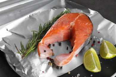 Photo of Aluminum foil with raw fish, lime, rosemary and spices on table, closeup. Baking salmon