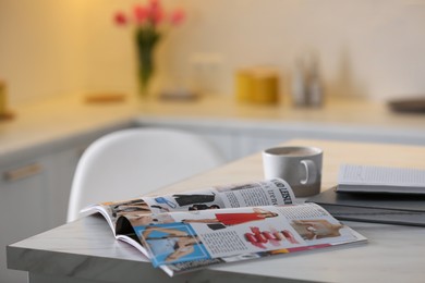 Photo of Open fashion magazine and drink on table in kitchen. Space for text
