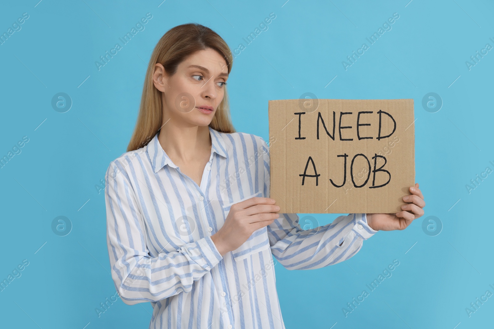 Photo of Unemployed woman holding sign with phrase I Need A job on light blue background