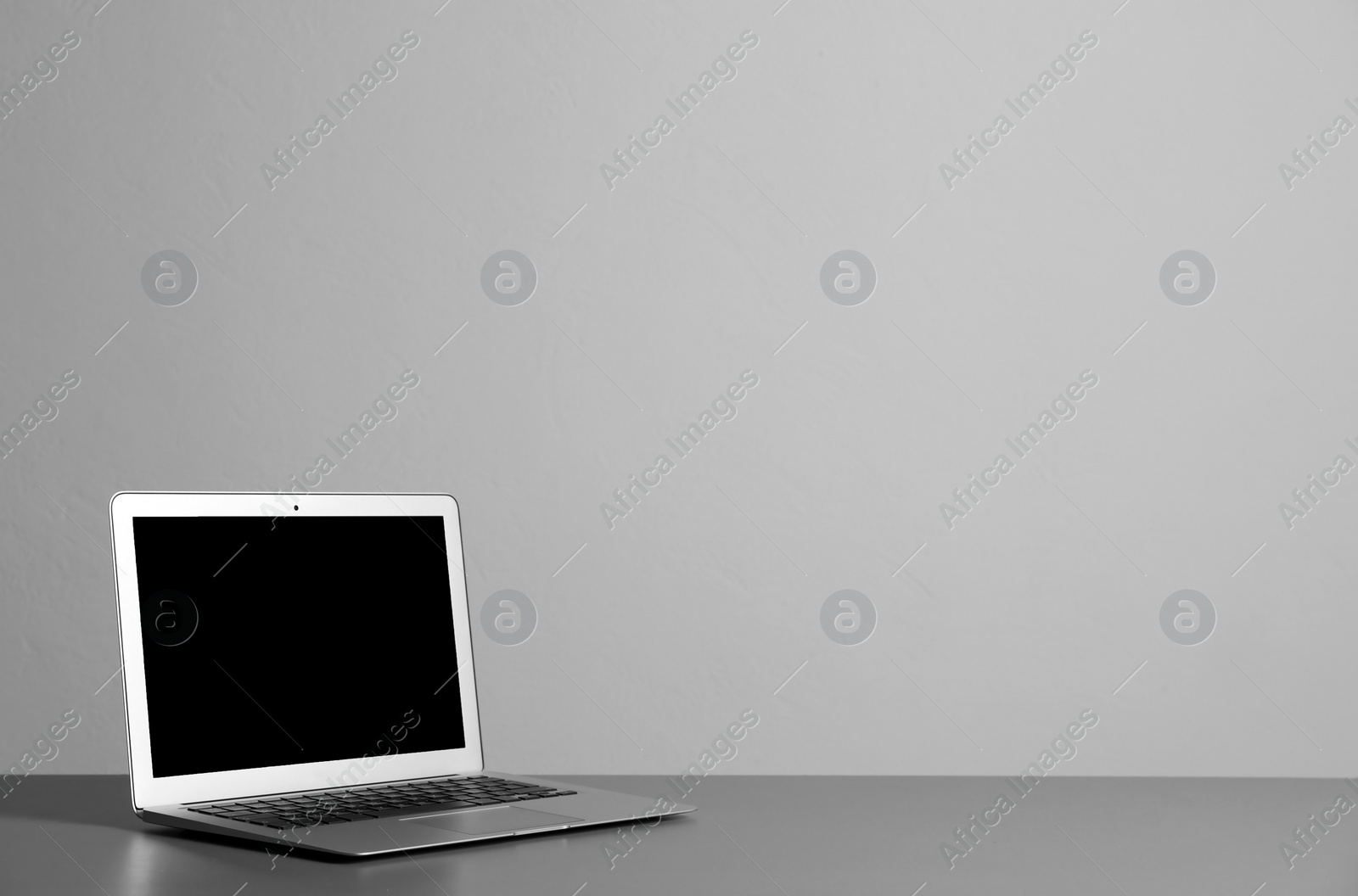 Photo of Modern laptop with blank screen on table against gray background