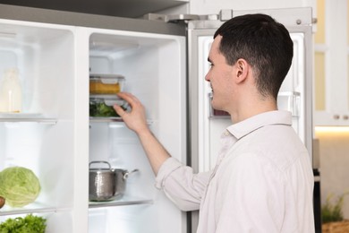 Photo of Happy man taking containers with vegetables out of refrigerator in kitchen