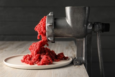 Metal meat grinder with beef mince on light wooden table