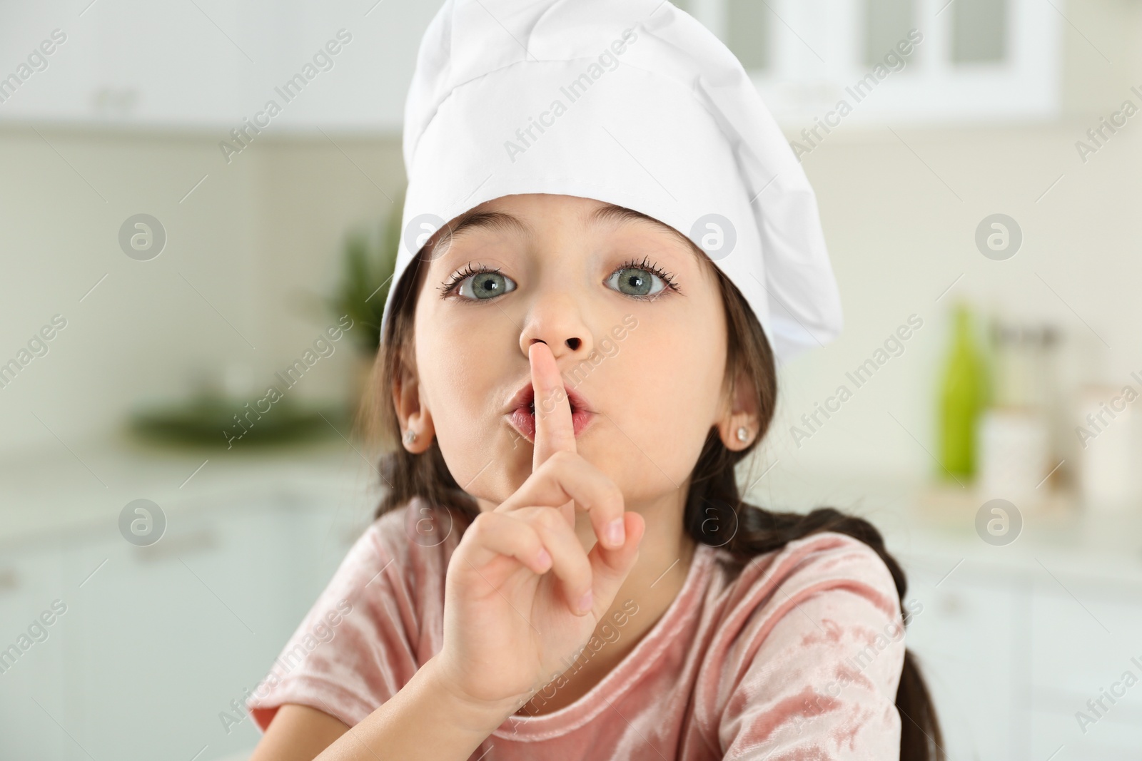 Photo of Cute little girl wearing chef hat in kitchen