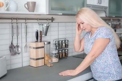 Photo of Mature woman suffering from headache in kitchen