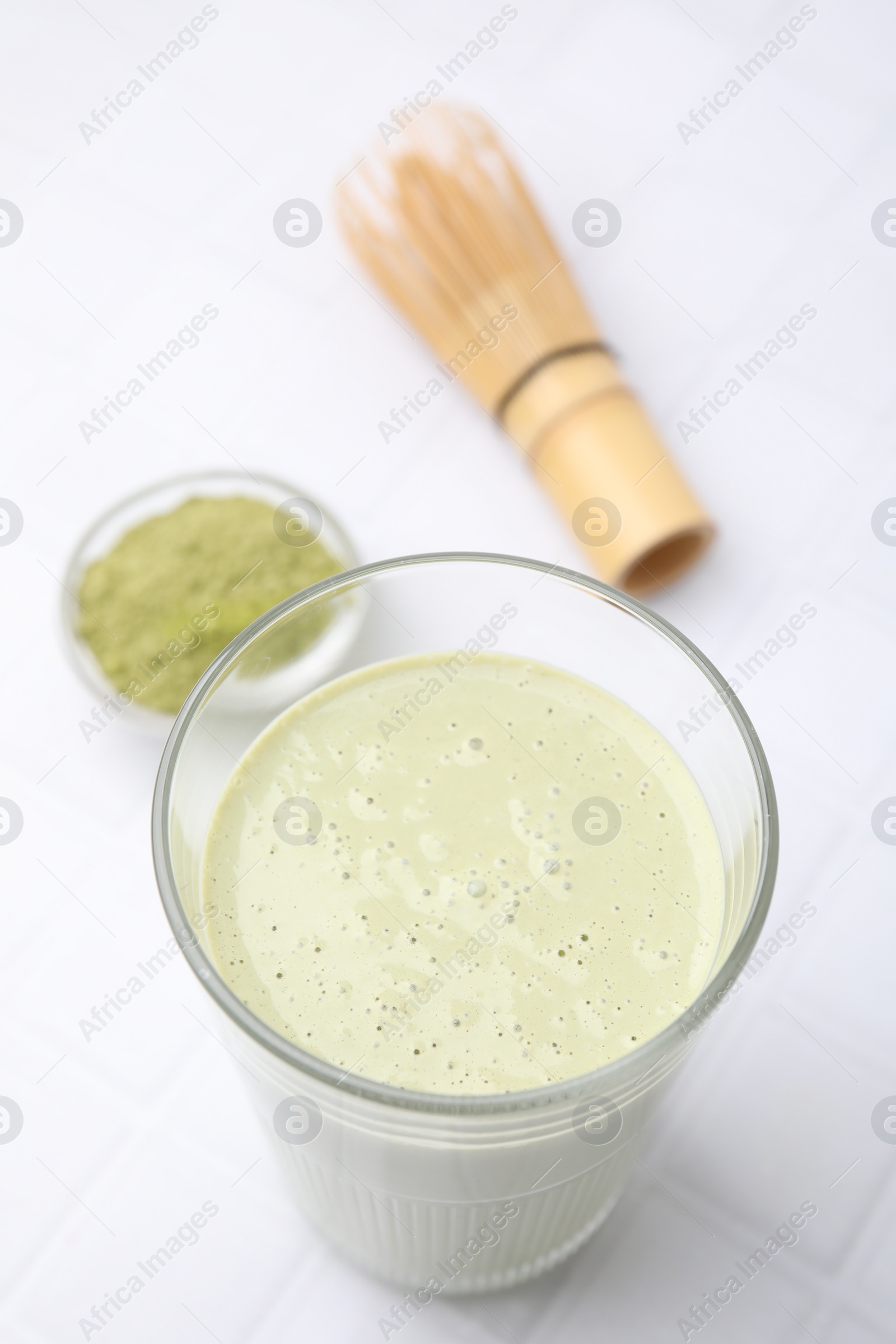 Photo of Glass of tasty matcha smoothie, powder and bamboo whisk on white tiled table, above view. Space for text