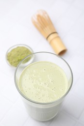 Glass of tasty matcha smoothie, powder and bamboo whisk on white tiled table, above view. Space for text