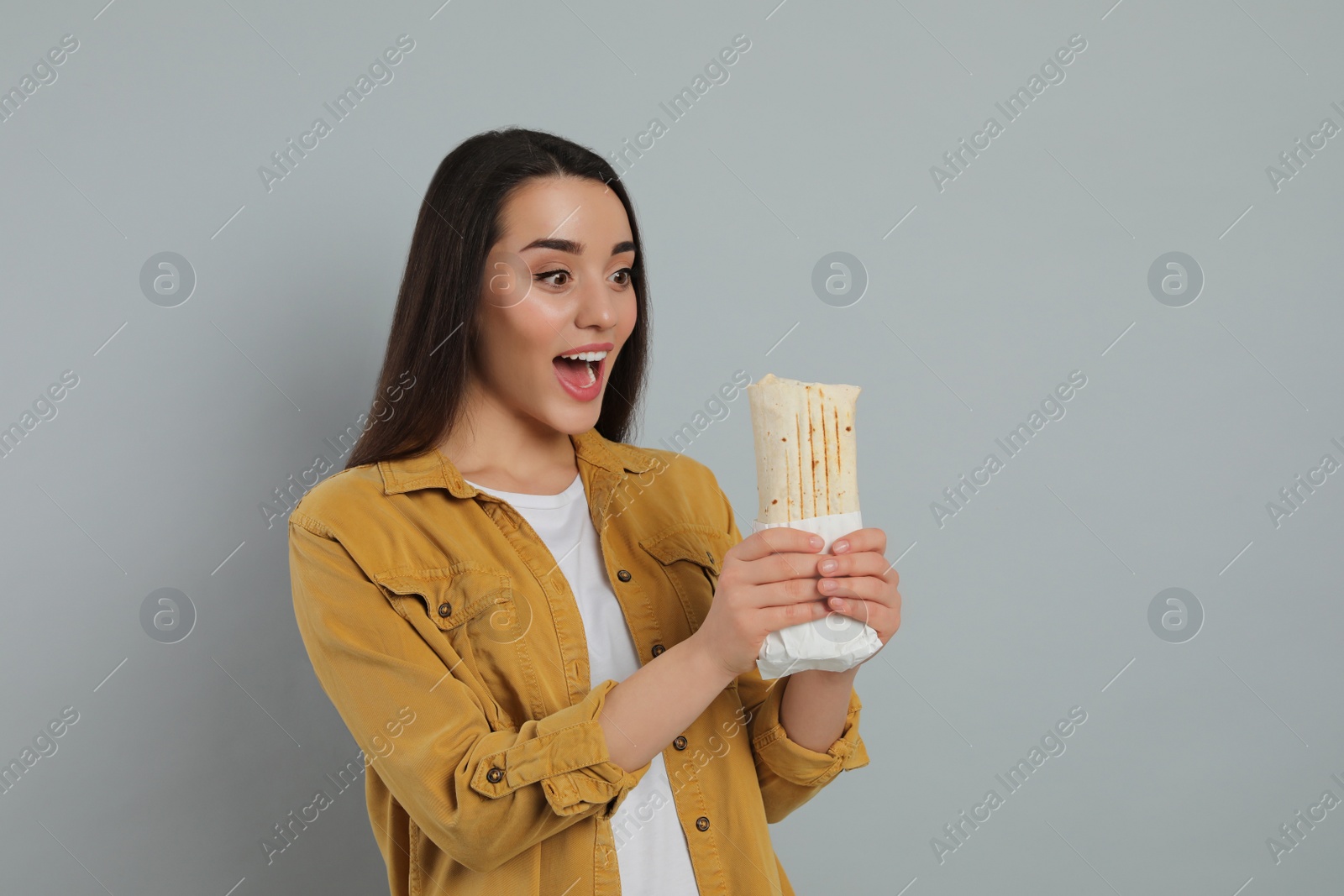 Photo of Happy young woman holding tasty shawarma on grey background