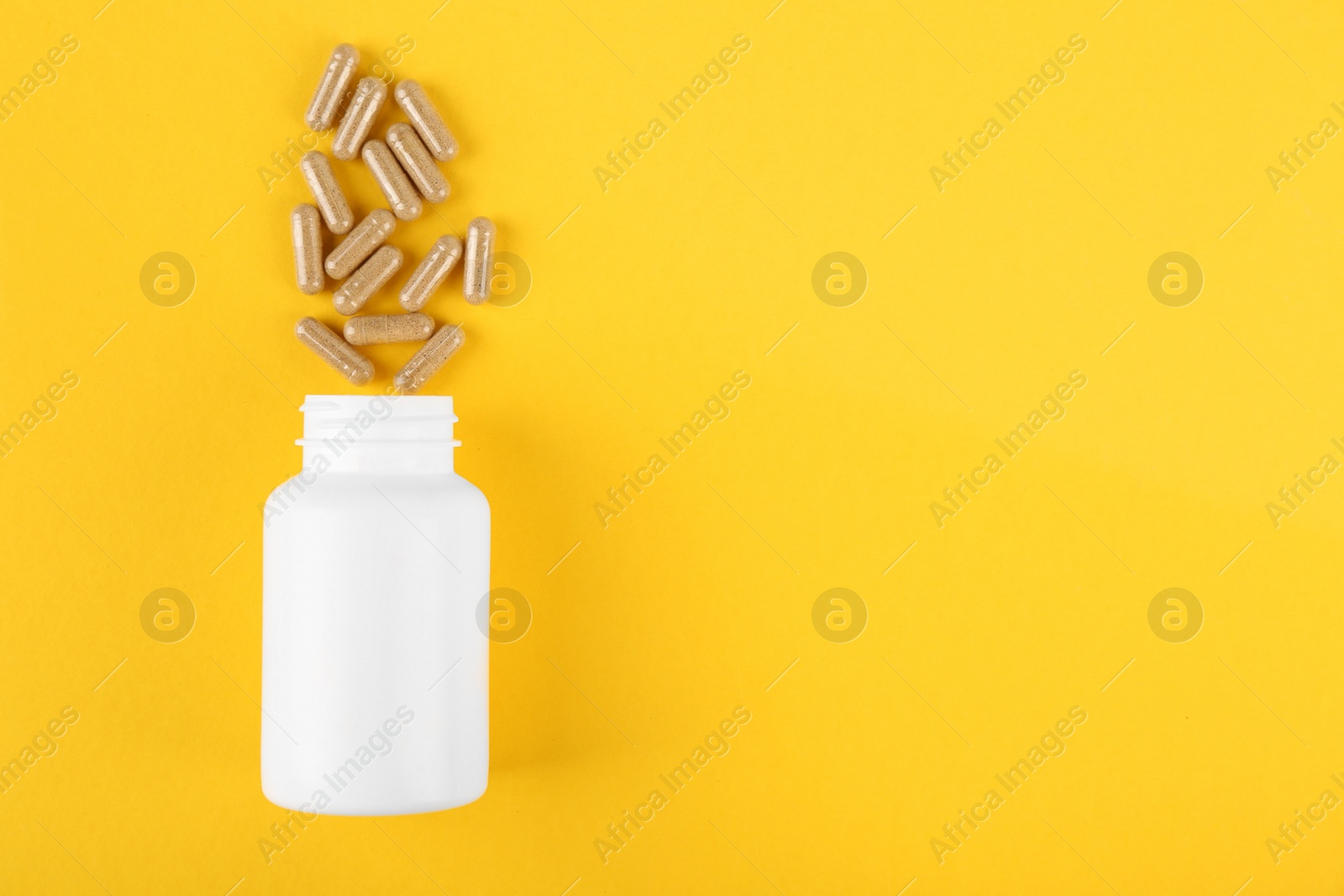 Photo of White medical bottle and vitamin capsules on yellow background, top view. Space for text