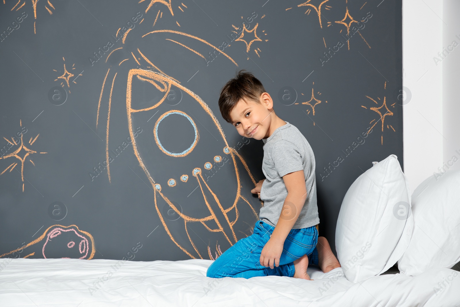 Photo of Little child drawing rocket with chalk on wall in bedroom