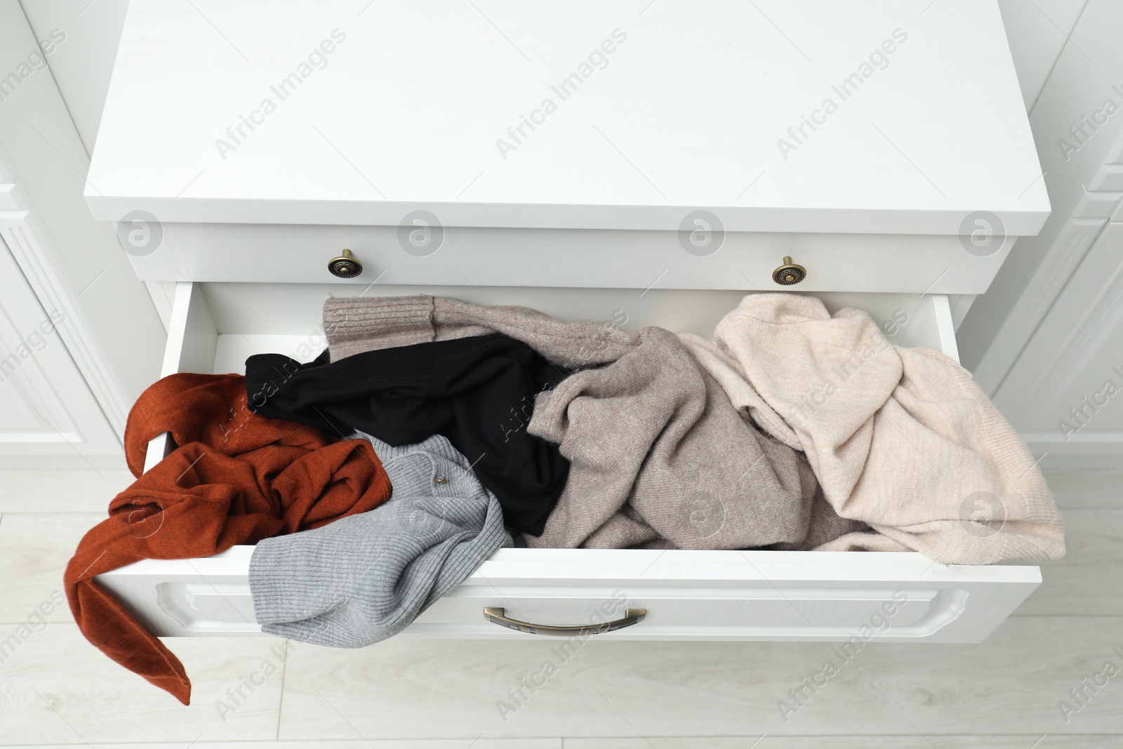 Photo of Cluttered chest of drawers indoors. Clothes in mess