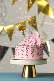 Photo of Beautifully decorated birthday cake and party decor on turquoise wooden table against blurred festive lights