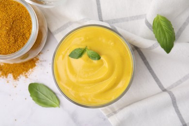 Photo of Tasty curry sauce, powder and basil leaves on white marble table, flat lay