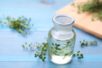 Bottle of thyme essential oil and fresh plant on light blue wooden table, closeup. Space for text