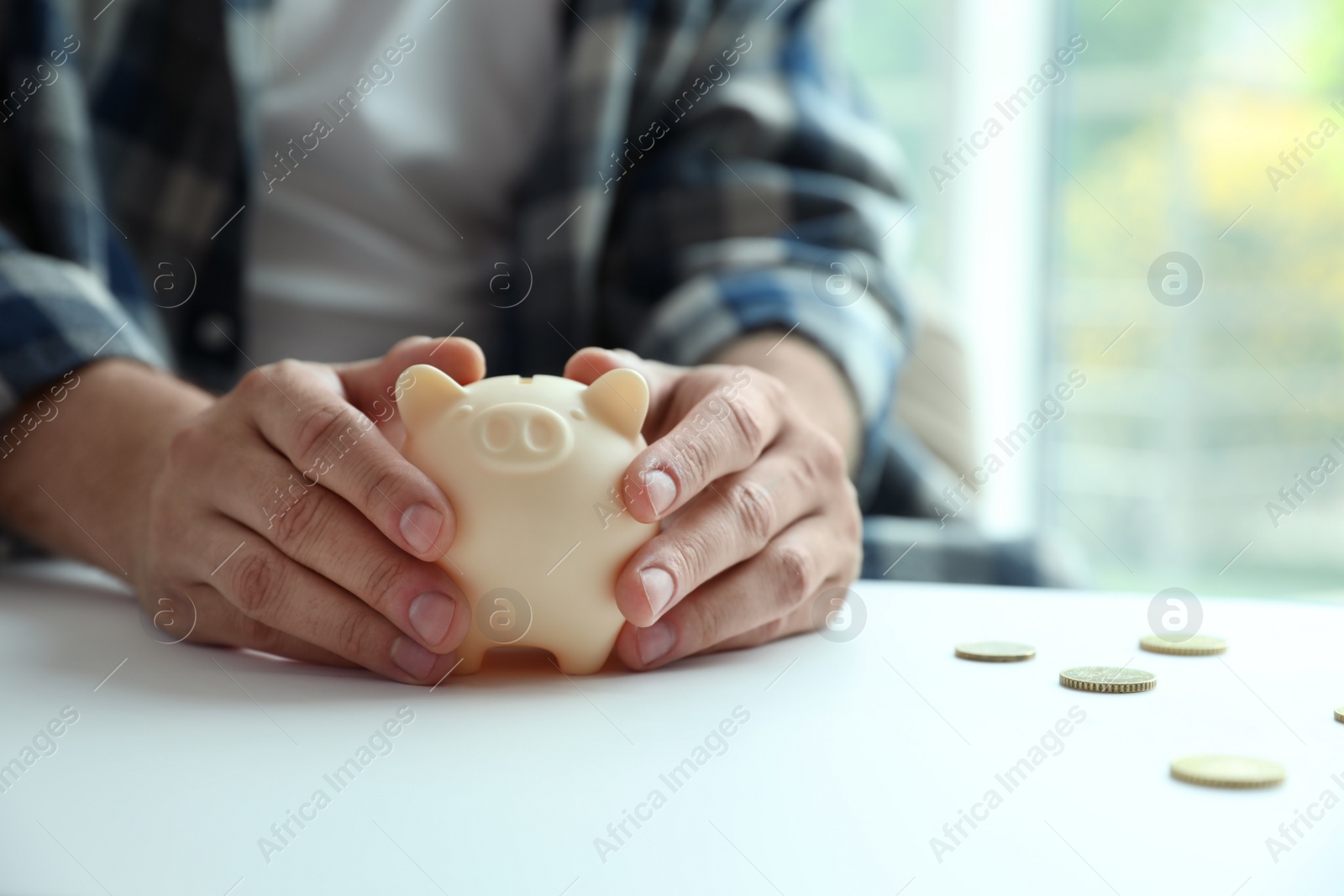 Photo of Man with piggy bank at white table against blurred background, closeup