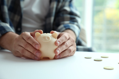 Man with piggy bank at white table against blurred background, closeup