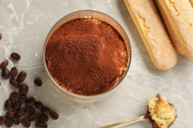 Photo of Tasty tiramisu in glass, coffee beans, spoon and biscuits on light grey table, flat lay