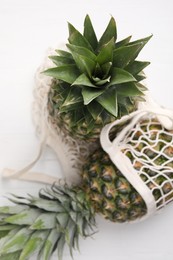 Net bag with delicious ripe pineapples on white wooden table, top view