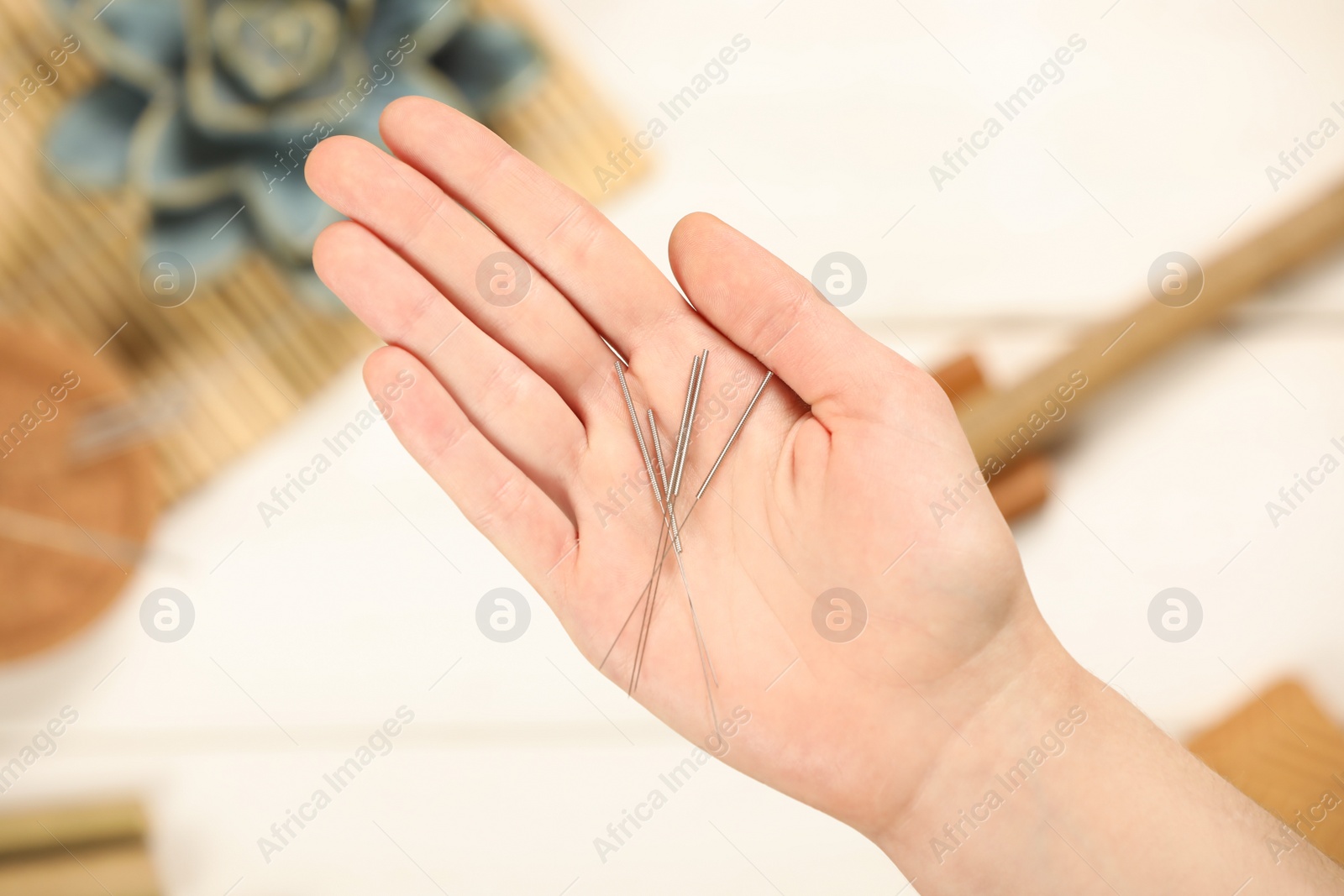 Photo of Woman holding many acupuncture needles over white wooden table, closeup