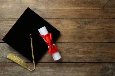Photo of Graduation hat and diploma on wooden table, flat lay. Space for text