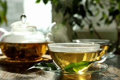 Fresh green tea in glass cups, leaves and teapot on wooden table
