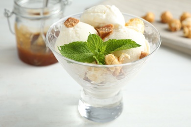 Delicious ice cream with caramel candies and popcorn in dessert bowl on white wooden table