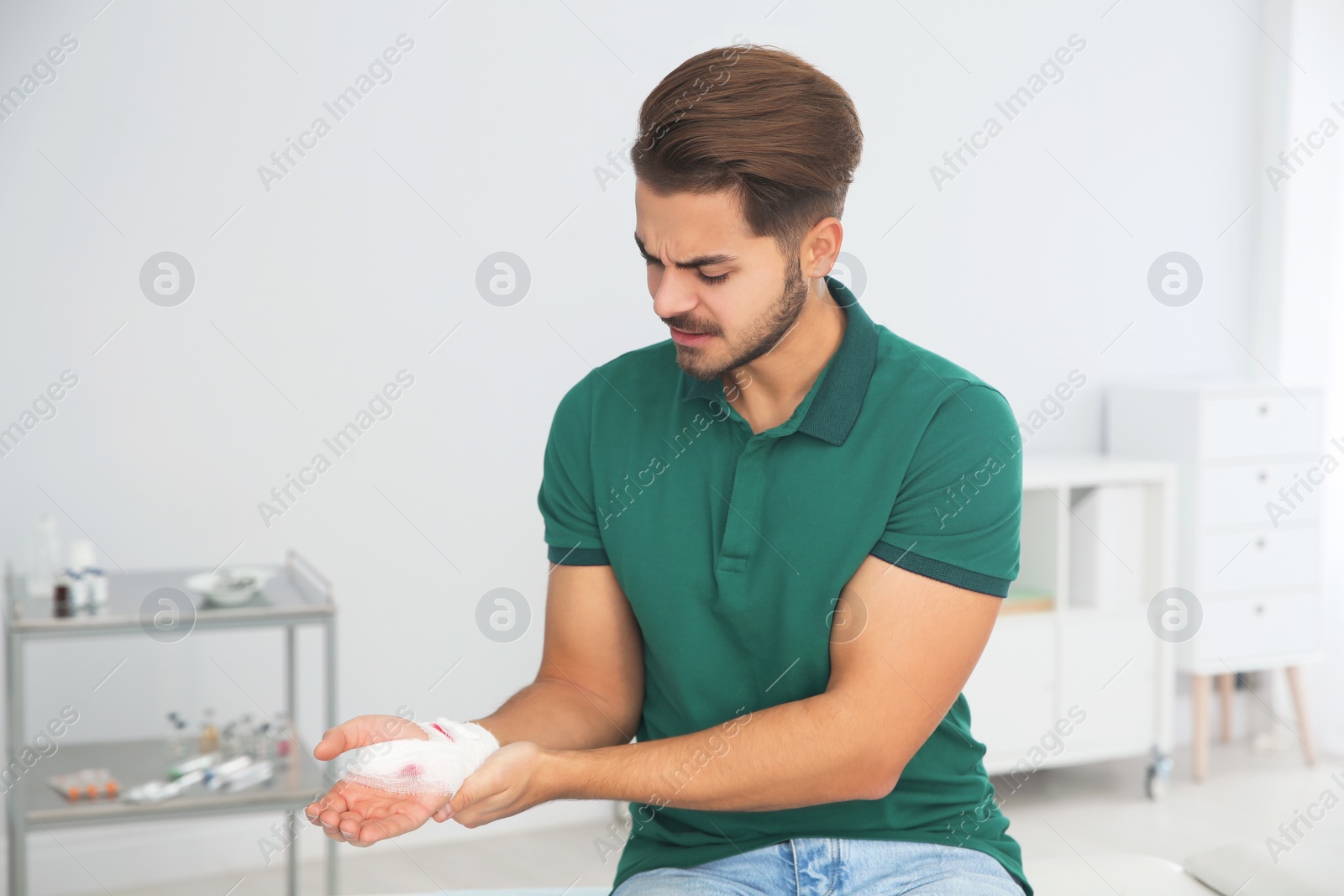 Photo of Young man with bandage on injured hand in clinic. First aid