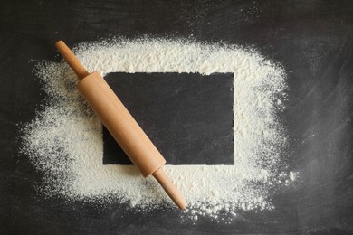 Flour and rolling pin on black table, top view